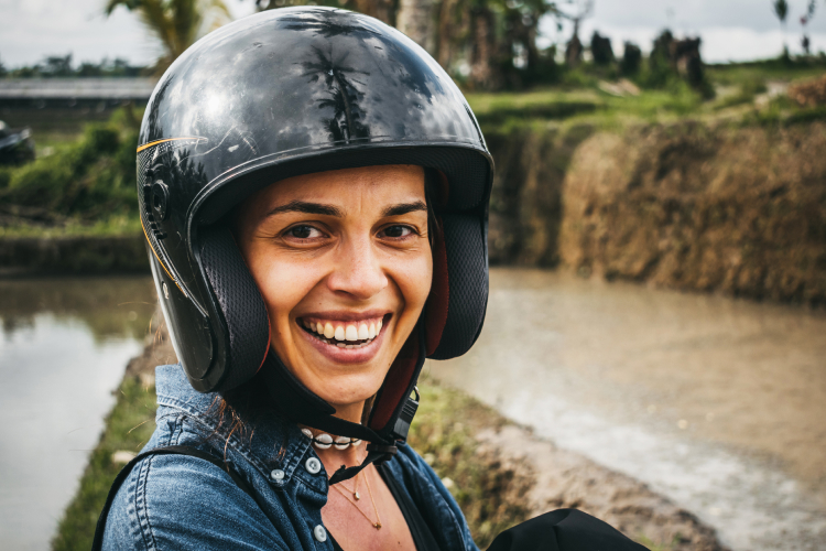 A smiling woman wearing a helmet in front of a rice field in Bali