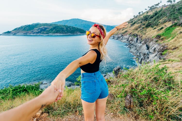 
Young woman holds hands out, on hillside above sea