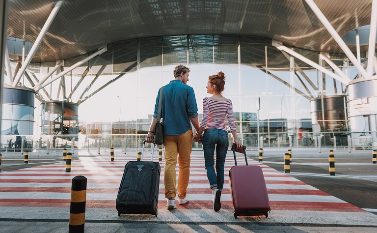 A couple holding hands and wheeling suitcases