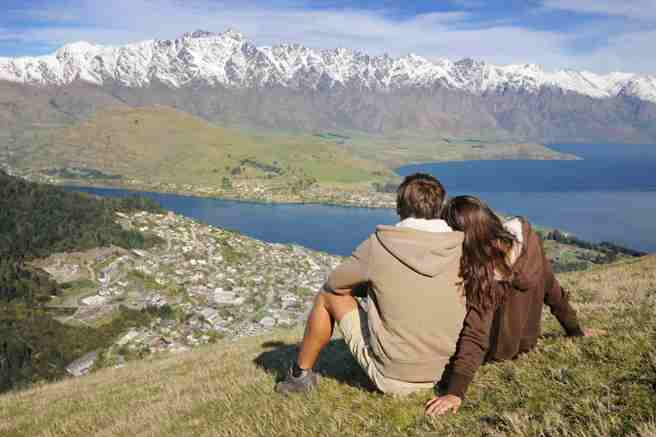 A couple sits on a hillside overlooking Queenstown, New Zealand. 