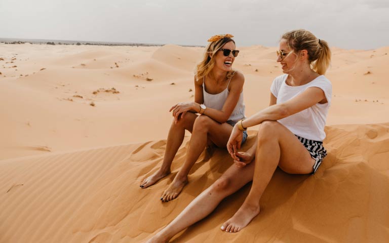 Two women sittin gon a sand dune