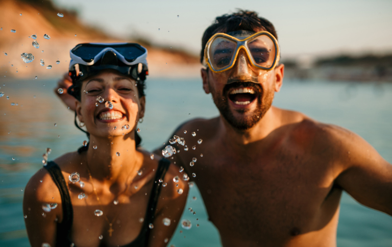 Two people smiling in the ocean wearing snorkel goggles